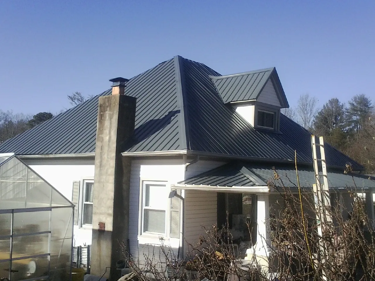 Dark blue standing seam metal roof on a white farmhouse with dormer — Slate & Tile Roof Repair by Roofing Brothers in Bradford