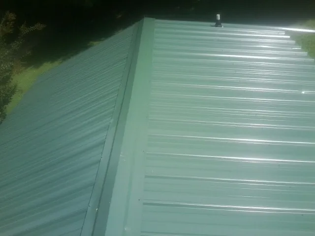 New green metal panels meeting at the ridge of a roof — Flat Roof Repair work by our crew in Bradford