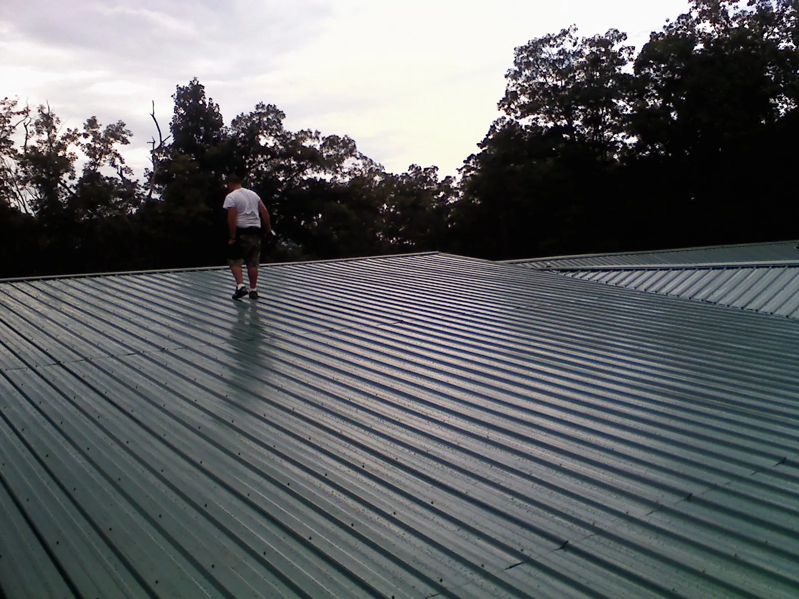 Roofer walking a wide expanse of new green metal roofing in Bradford