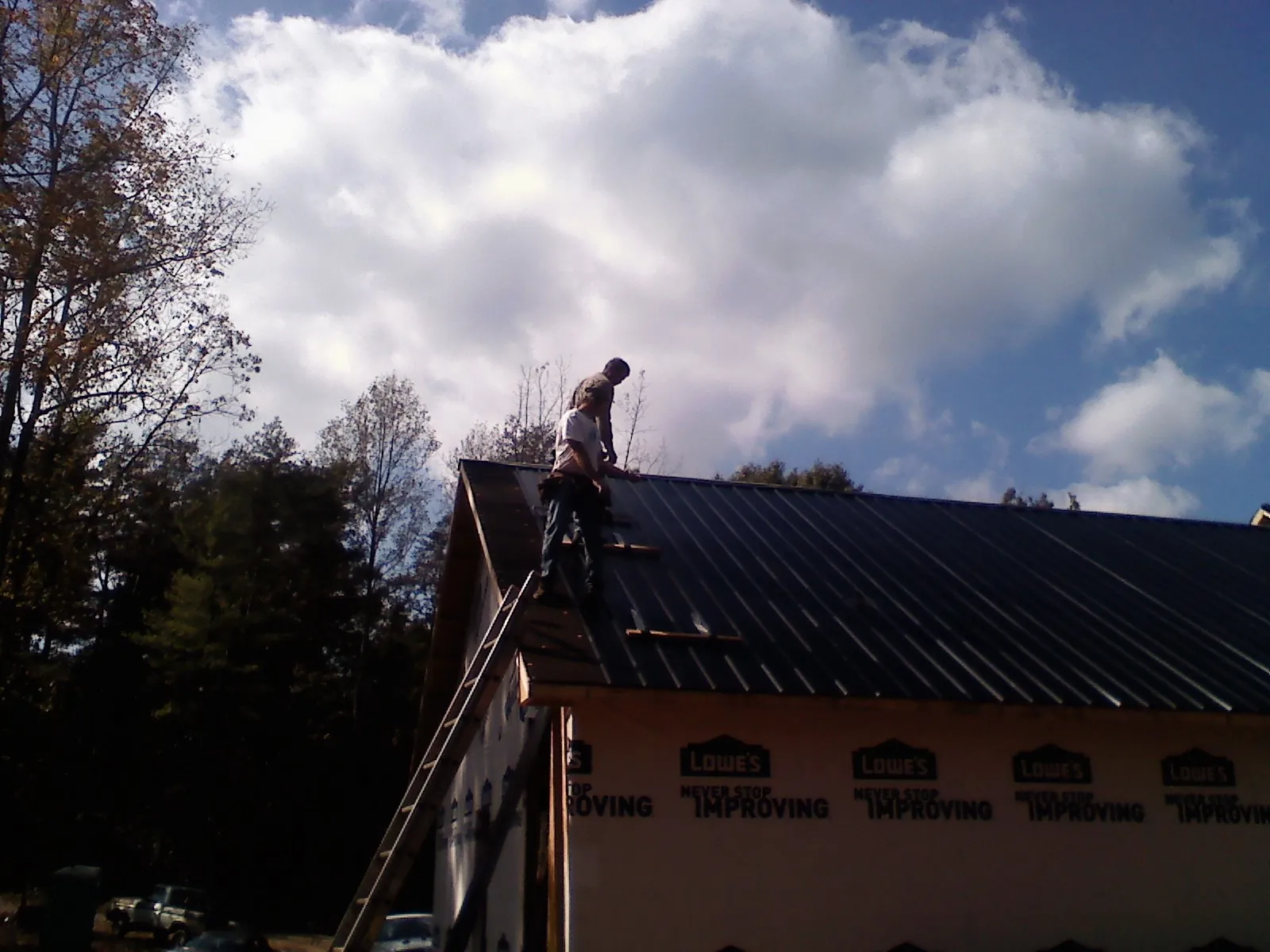 Roofer fastening dark metal panels high against a cloudy sky, from a Roof Inspection job in Bradford